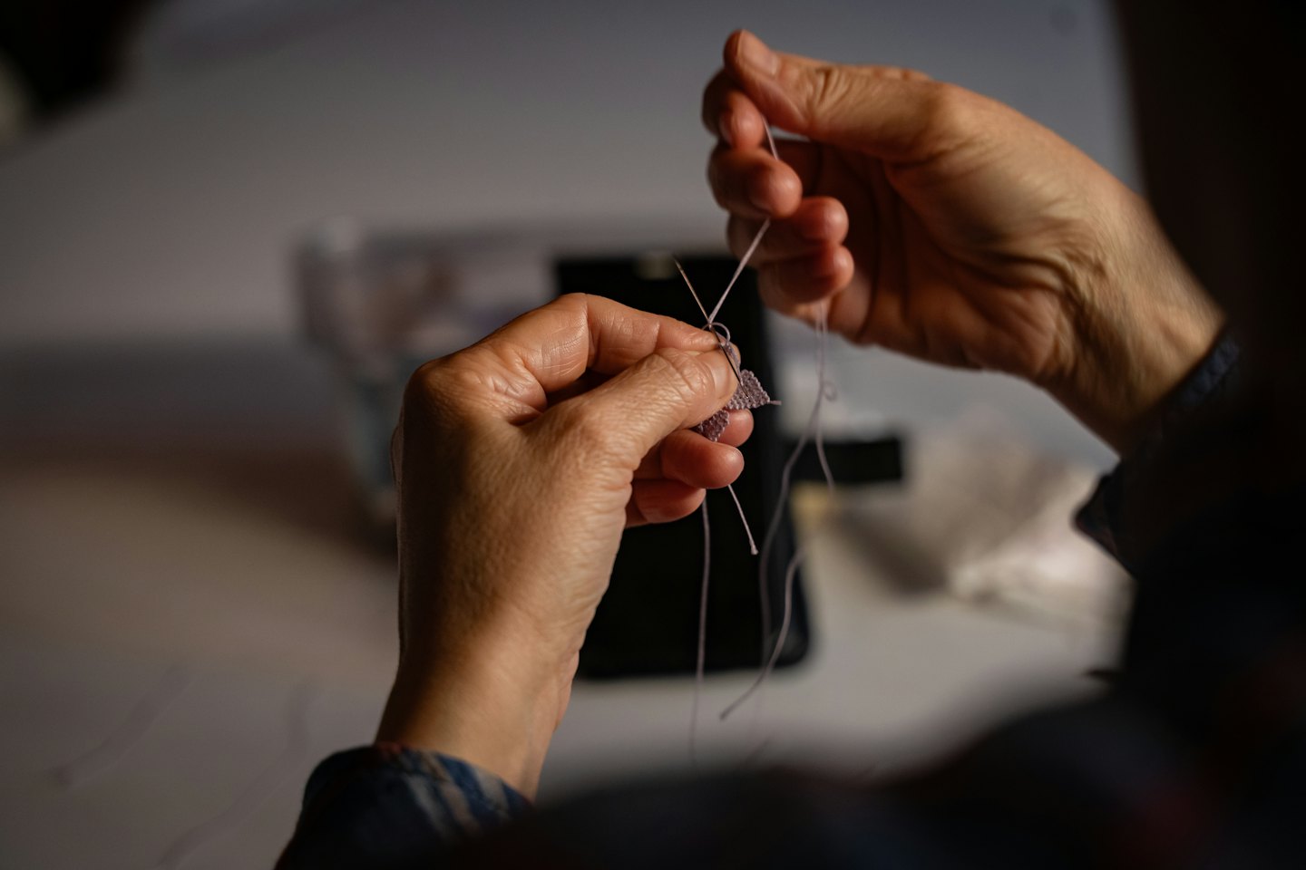 Hands carefully working on a detailed lavender needlework project.