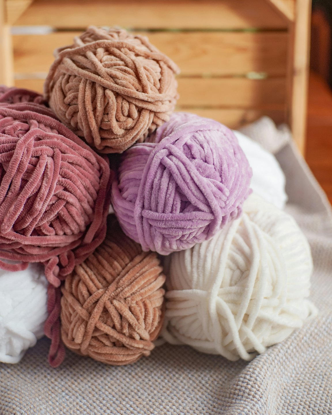 Pastel chenille yarn balls resting on a textured blanket.