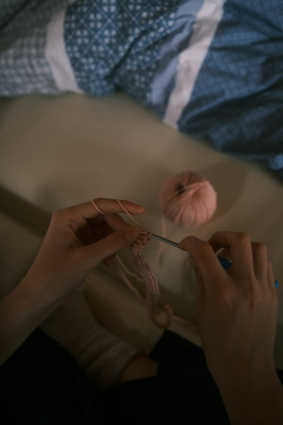 Hands crochet a project with pink yarn and a hook.